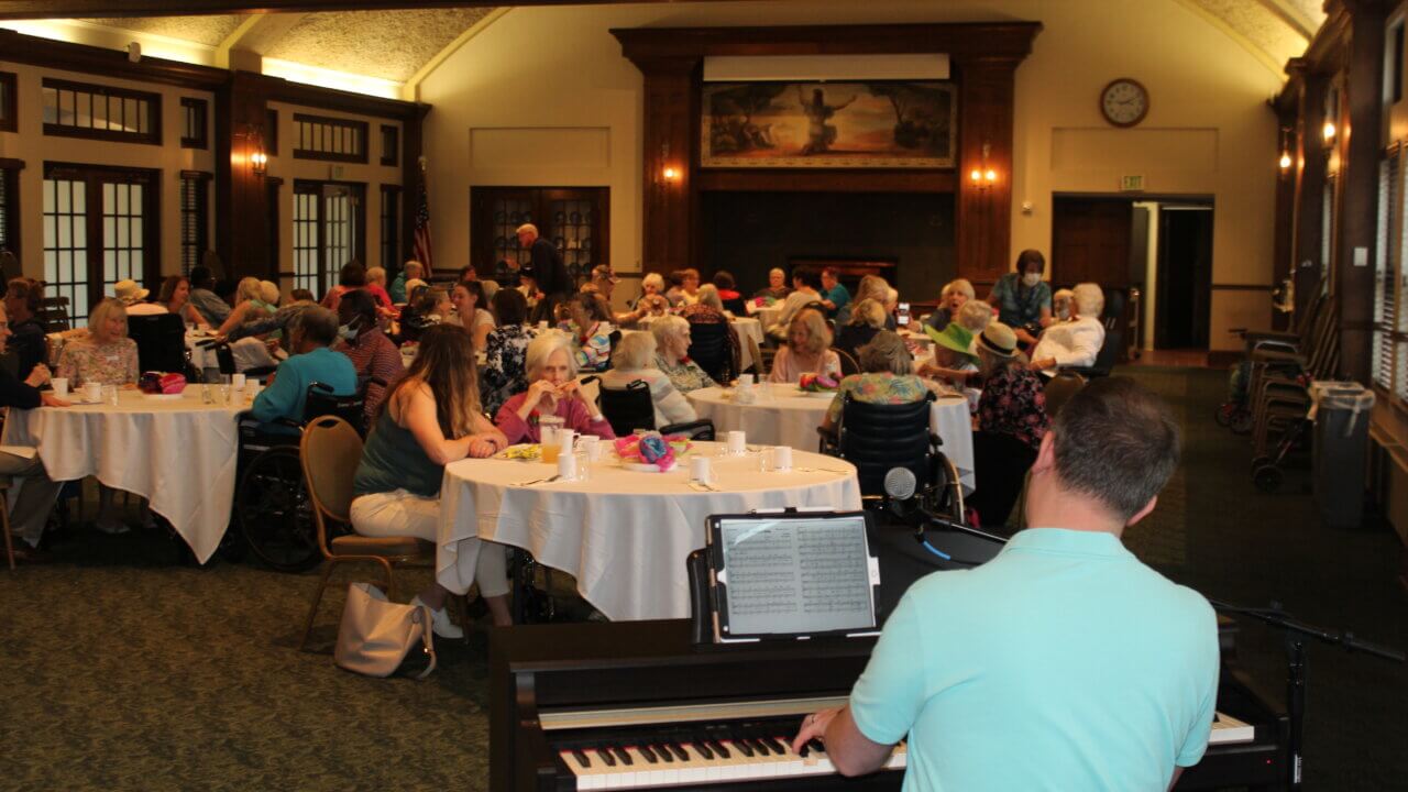 Gathering of people at tables while a person plays piano